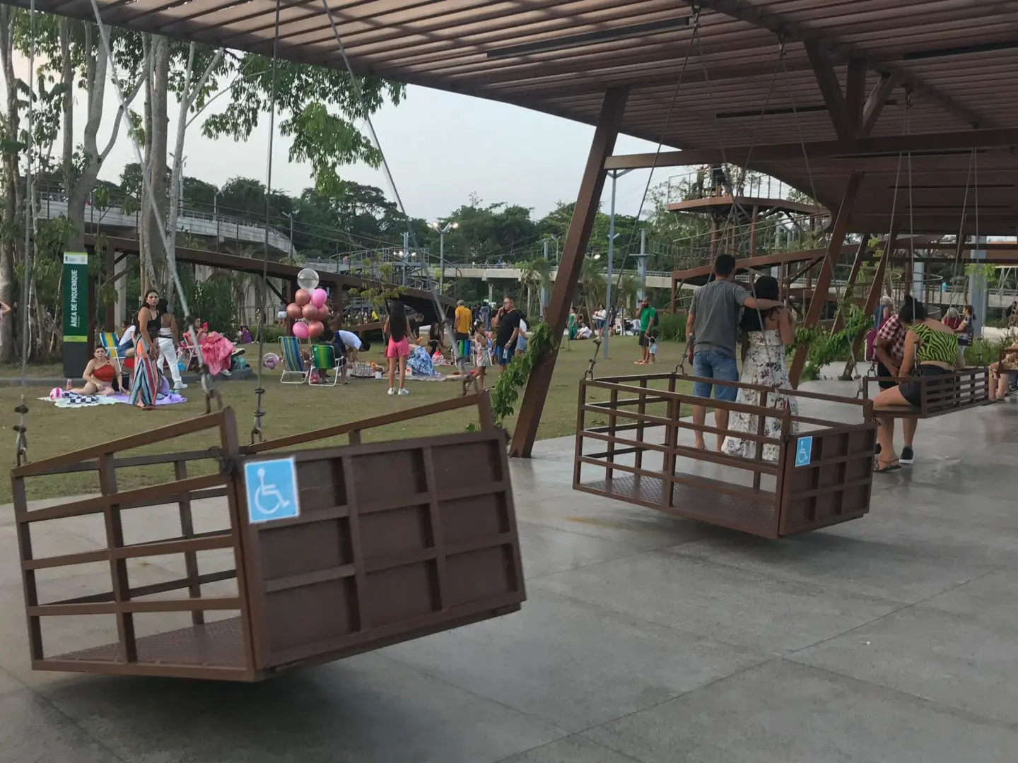 Imagem de parquinhoa inclusivos mostra o espaço do Parque Maguary, com área de balanço de madeira para cadeirantes. 