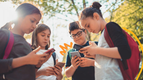 Um grupo de adolescentes está reunido e todos olham para a tela dos respectivos celulares. A matéria fala sobre o Jogo do Tigrinho nas escolas.