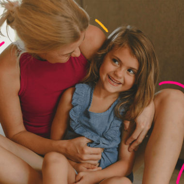 Imagem para capa de matéria sobre parentalidade positiva mostra uma mulher loira sentada no chão de uma casa com uma menina branca de cabelos lisos no colo.