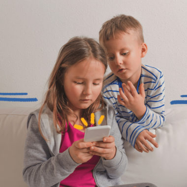 Imagem de capa para matéria sobre a pesquisa Tic Kids Online mostra duas crianças, uma menina e um menino, usando um celular e sentados em um sofá.