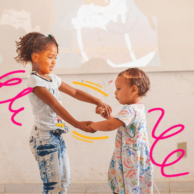 Imagem mostra duas crianças das favelas da Maré brincando. Um menina negra de cabelos crespos e roupa scoloridas segura a mãe de uma menina bebê.