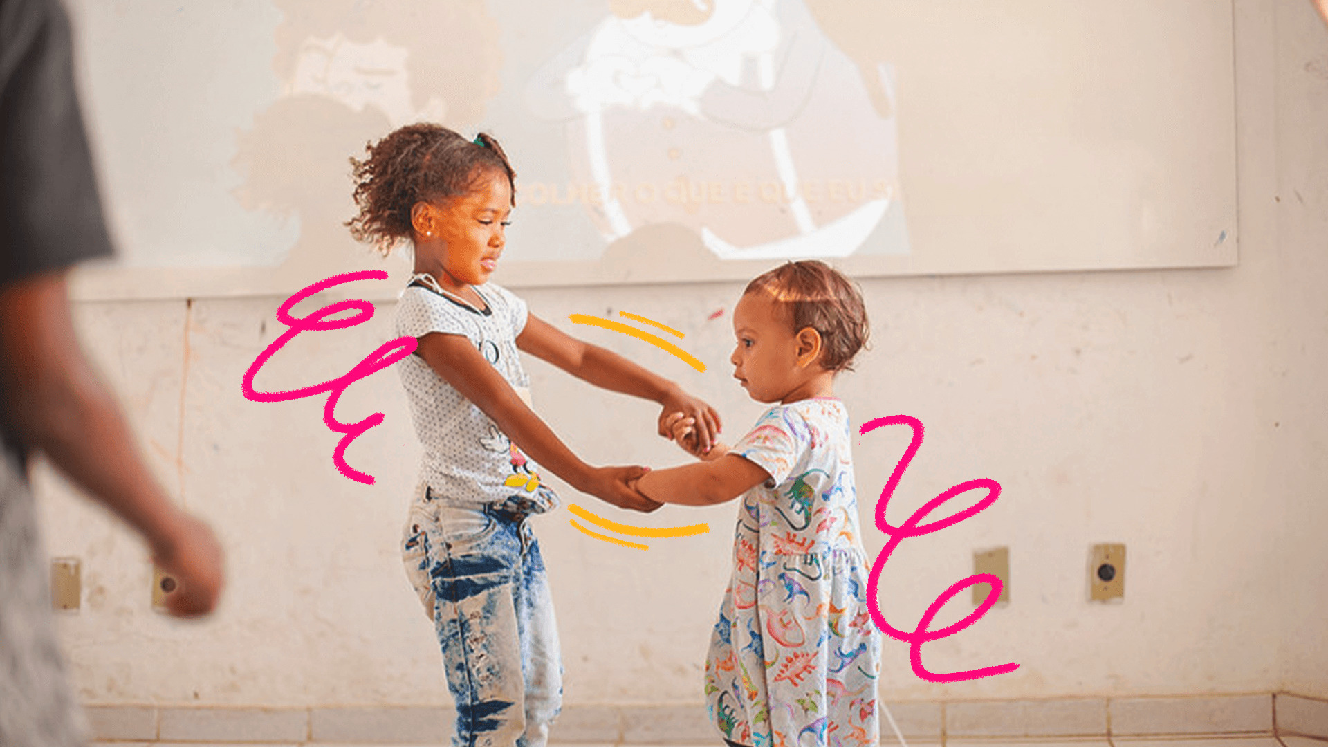 Imagem mostra duas crianças das favelas da Maré brincando. Um menina negra de cabelos crespos e roupa scoloridas segura a mãe de uma menina bebê.