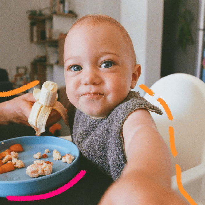 Imagem de capa mostra um bebê branco, sentado em um cadeirão de alimentação e comendo uma banana.