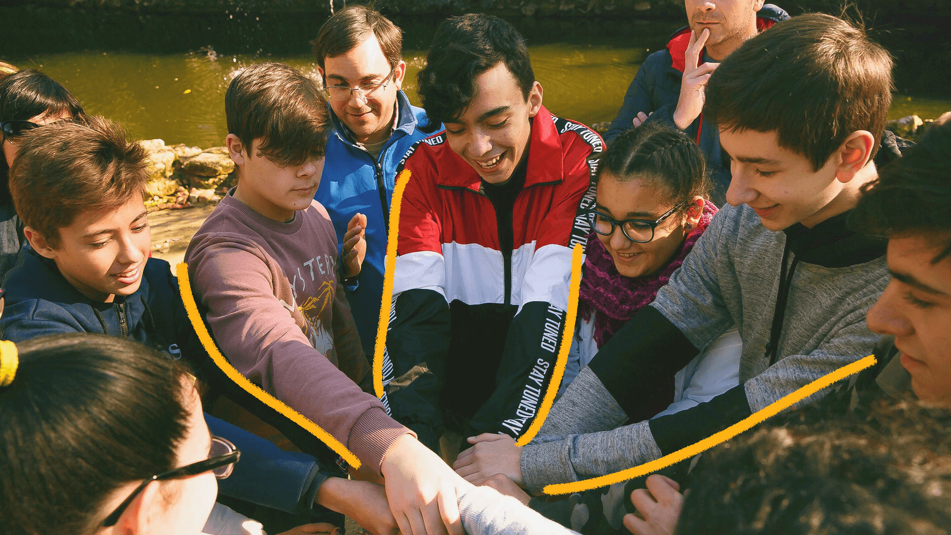 Imagem mostra um grupo de adolescentes vestindo roupas coloridas e unindo as mãos em uma roda.