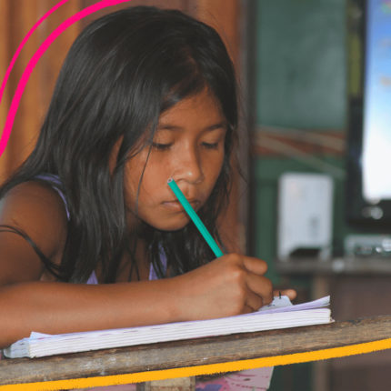 Imagem de capa para matéria sobre educação indígena no Pará mostra uma menina indígena sentada em uma carteira e escrevendo em um caderno, em uma sala de aula.