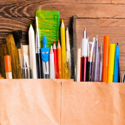 Imagem de capa para matéria sobre reutilização de material escolar mostra uma sacola de papel com vários objetos de escola como lápis e canetas.