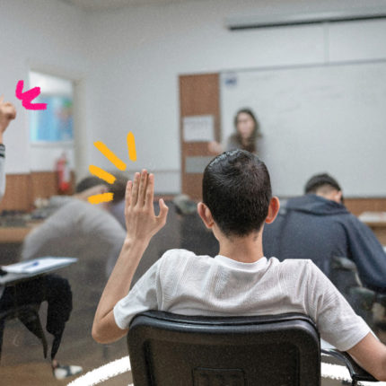 Imagem de capa para matéria sobre lei que proíbe celulares nas escolas mostra uma sala de aula e estudantes sentados em carteiras enquanto um aluno adolescente está com a mão levantada.