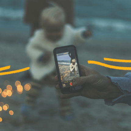 Imagem de capa para matéria sobre sharenting mostra uma mão de um aduto segurando um celular com a câmera apontada para um bebe em uma praia.