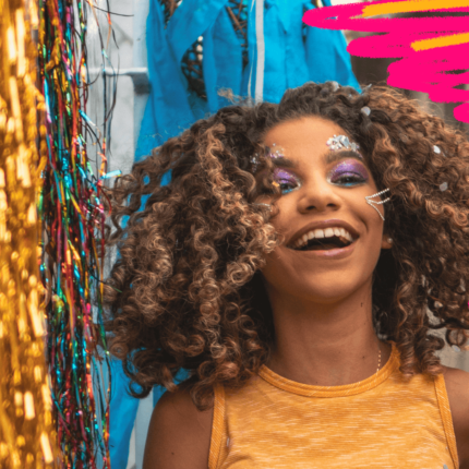 Carnaval com proteção: imagem de capa mostra uma menina negra de cabelhos cacheados sorrindo em meio a fantasias de carnaval.