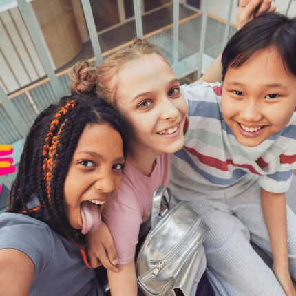 Imagem de capa para matéria sobre o que as meninas dizem no 8 de março mostra três meninas, uma negra, uma loira e uam oriental. Elas estão sentadas e sorrindo para a foto.