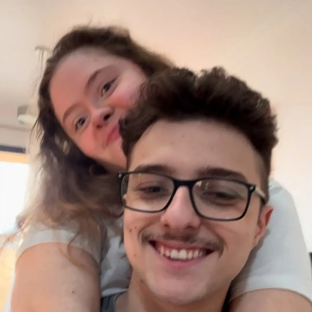 Imagem mostra Lívia, uma adolescente branca com Síndrome de Down e Augusto, um jovem branco, de óculos e cabelos curtos. 