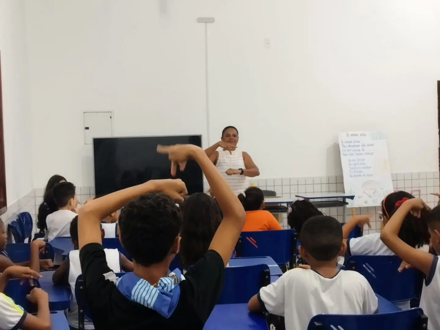 Imagem mostra professora ensinando libras em sala de aula para crianças.