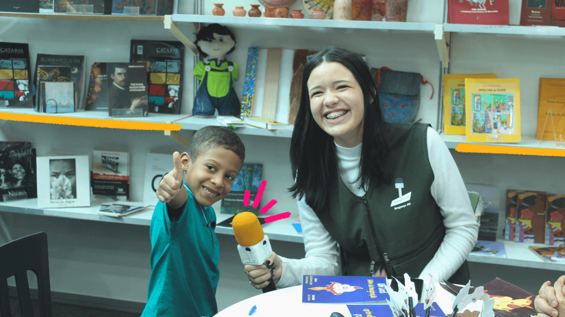 Imagem mostra adolescente de projeto de comunicação entrevistando criança com um microfone.