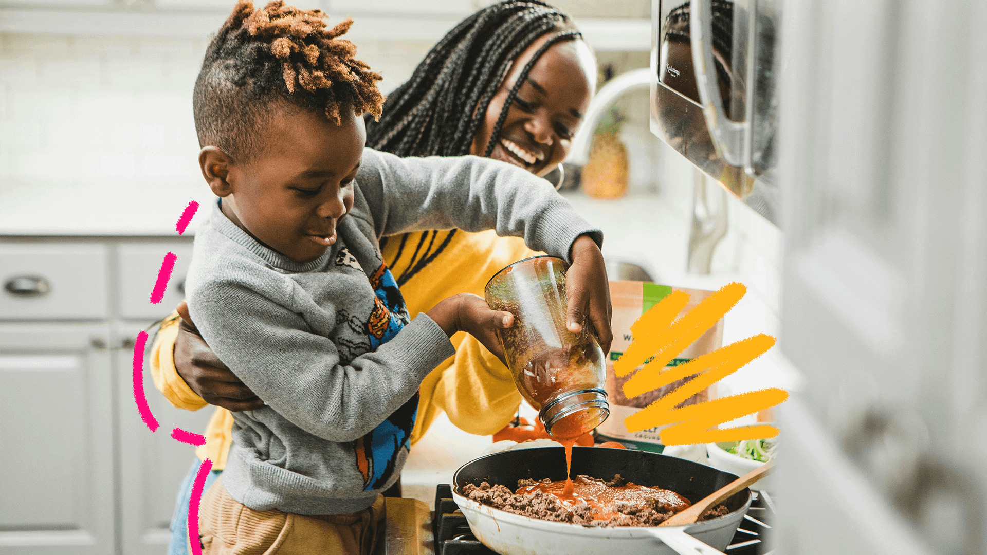 Uma mulher negra de tranças no cabelo e blusa amarelo ajuda um menino negro de blusa cinza a preparar uma comida na frigideira