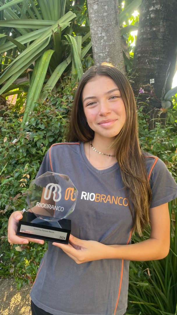 imagem mostra uma adolescentes branca, de cabelos longos, segurando um troféu.