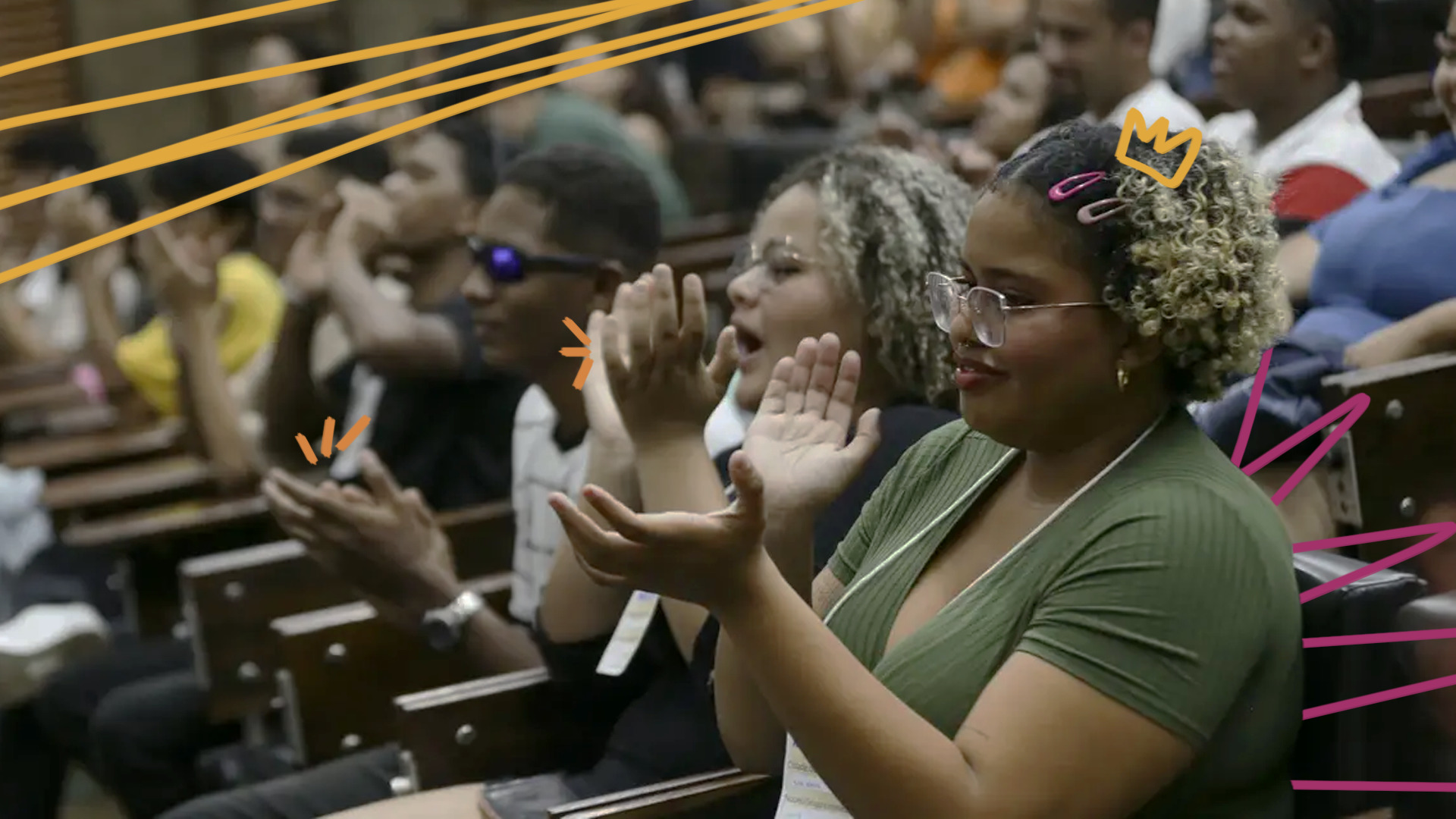 Imagem mostra um grupo de estudantes adolescentes negros sentados em um auditório e aplaudindo.