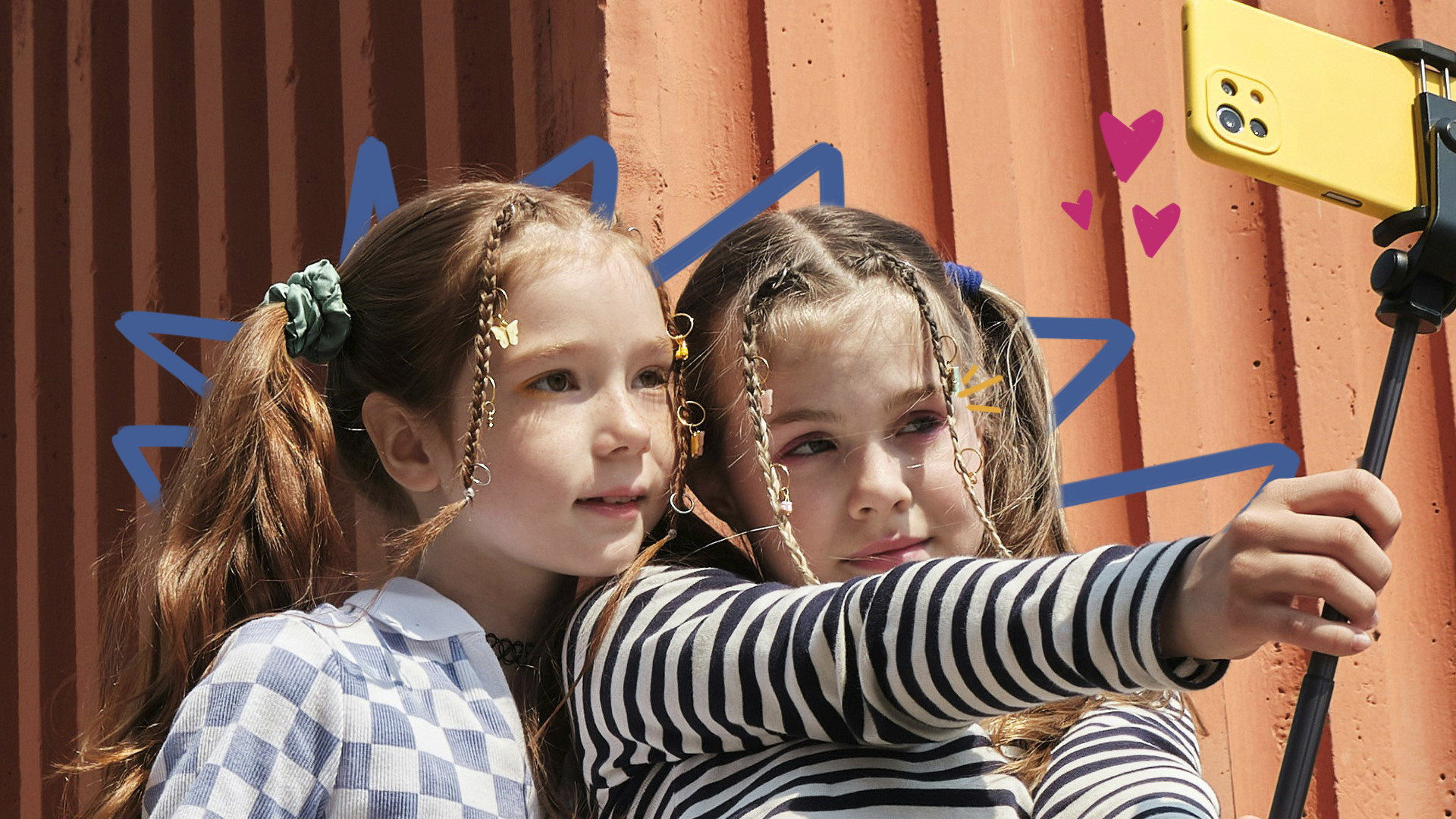participação infantil - Imagem mostra duas meninas brancas com tranças no cabelo fazendo selfie com um celular.