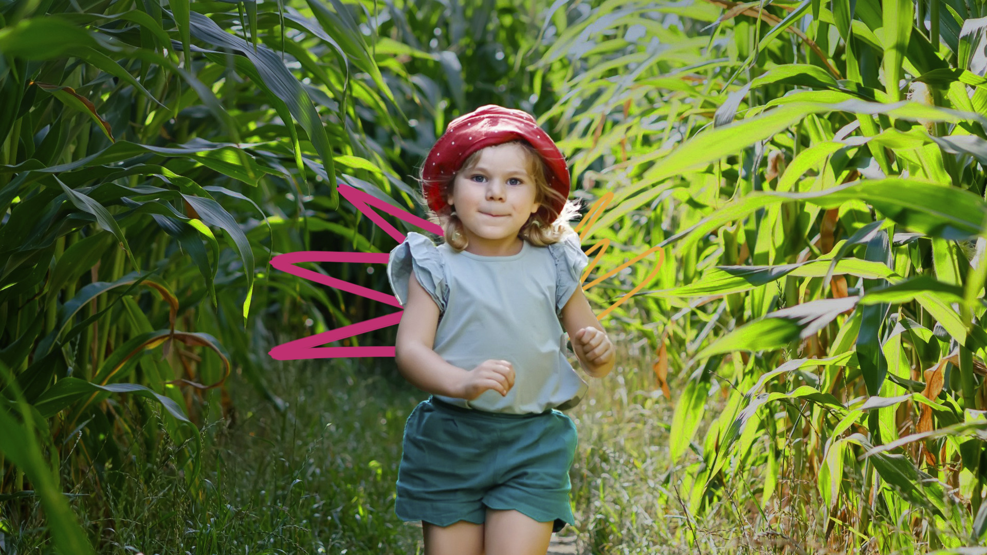 Uma menina de pele e cabelo claros está em meio a plantas, usa short, blusa e um chapéu vermelho.