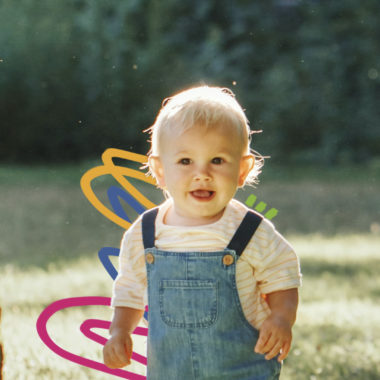 Um bebê de pele e cabelo claro está ao ar livre usando uma jardineira jeans e blusa branca.