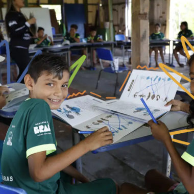 Três crianças de uniforme verde fazem um trabalho em grupo