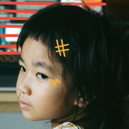 Uma menina de traços orientais e cabelos escuros está de perfil e há um computador à sua frente