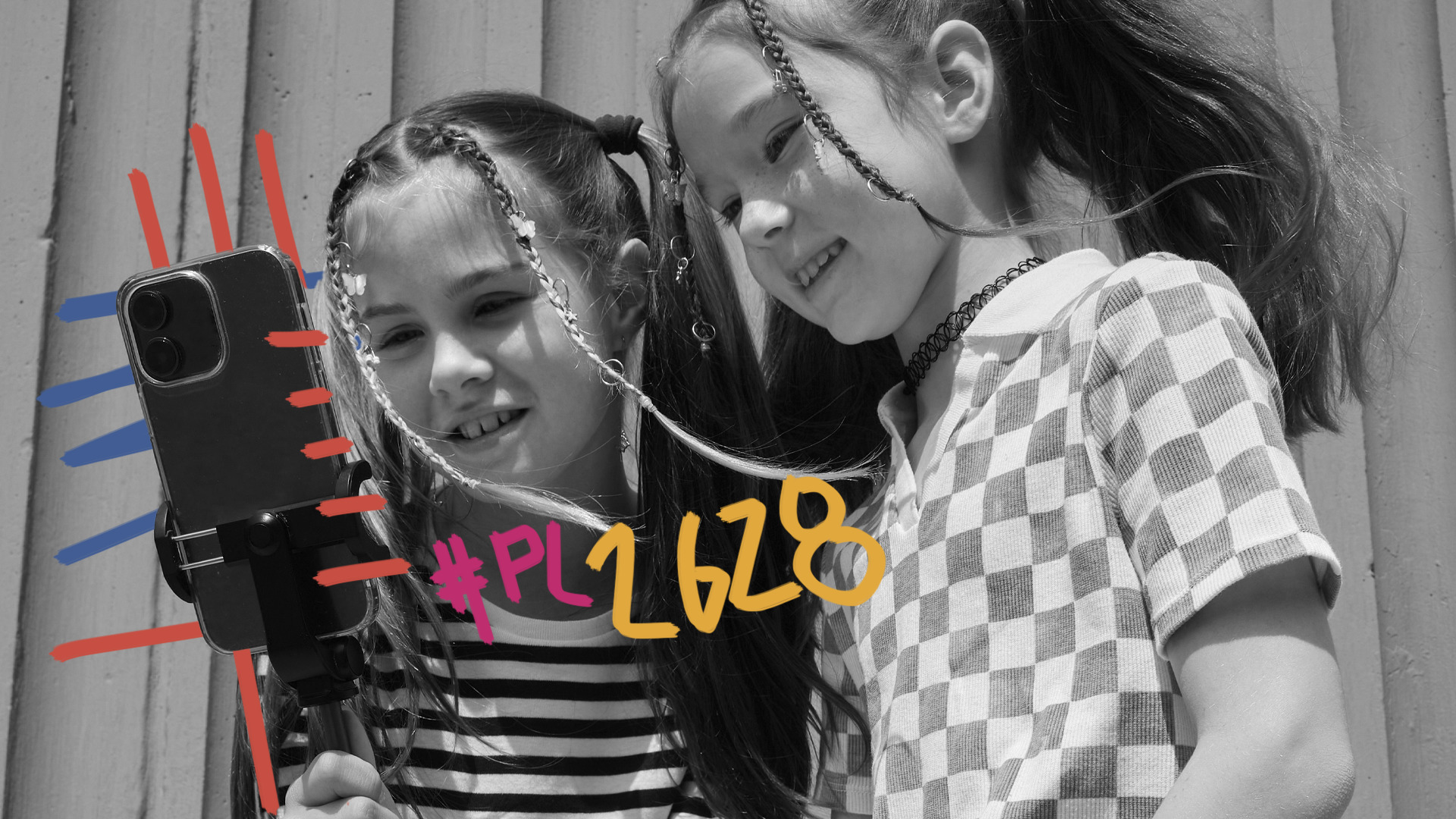 Foto em preto e branco de duas meninas olham para a tela de um celular. Uma delas está com blusa listrada e a outra quadriculada. Na imagem, há o texto: #PL2628