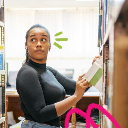 Imagem mostra uma mulher negra vestindo blusa preta em uma biblioteca.