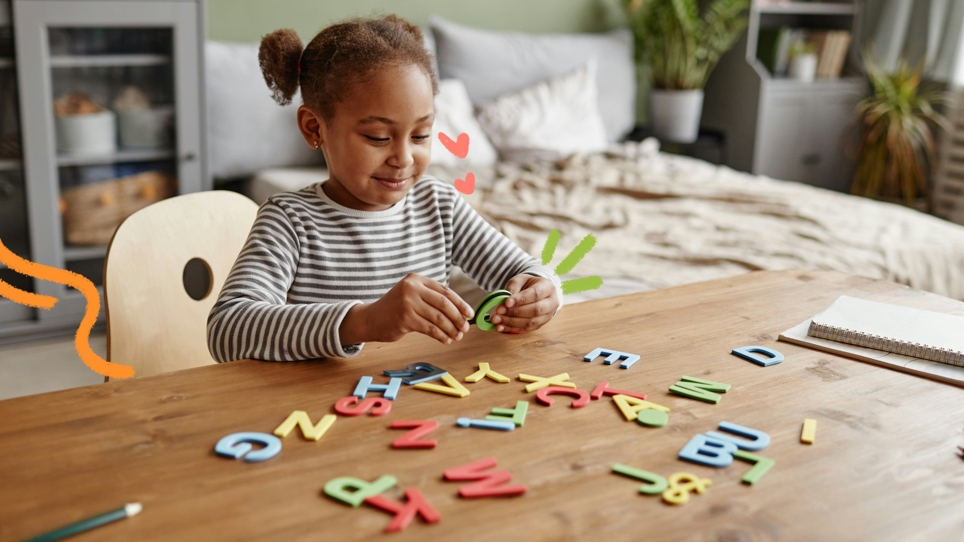 Uma menina negra de coque e blusa listrada está brincando com letras coloridas dispostas em uma mesa de madeira na sala de casa.