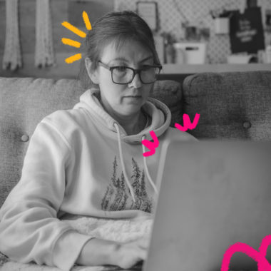 Diagnóstico de internet: Imagem mostra uma mulher sentada branca, de cabelos lisos presos, óculos e moleton, sentada em um sofá e usando um notebook.