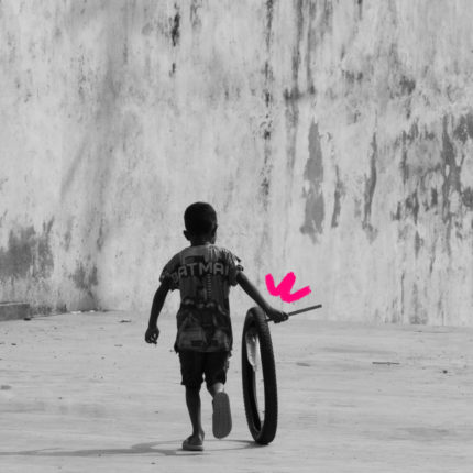 Imagem de capa para matéria sobre brincadeiras para brincar até cansar mostra um menino negro brincando na rua com uma roda de bicicleta.