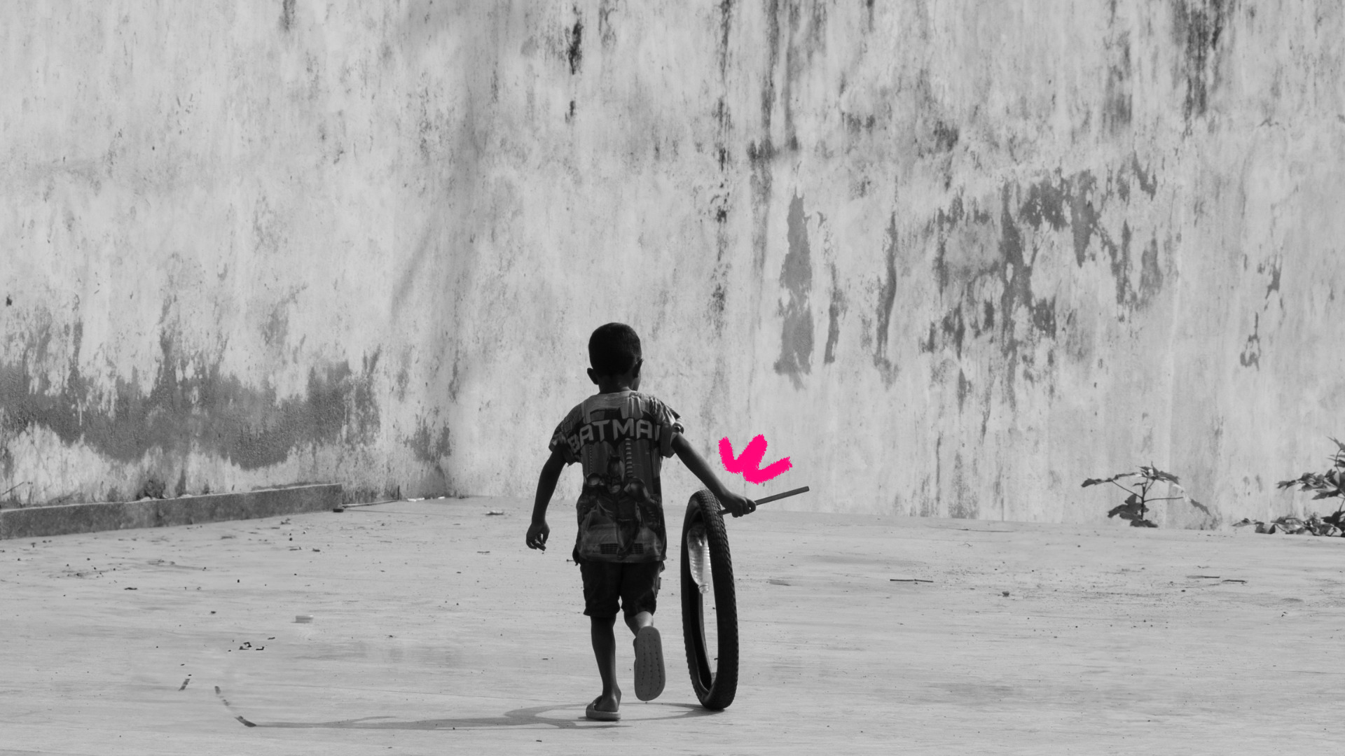 Imagem de capa para matéria sobre brincadeiras para brincar até cansar mostra um menino negro brincando na rua com uma roda de bicicleta.