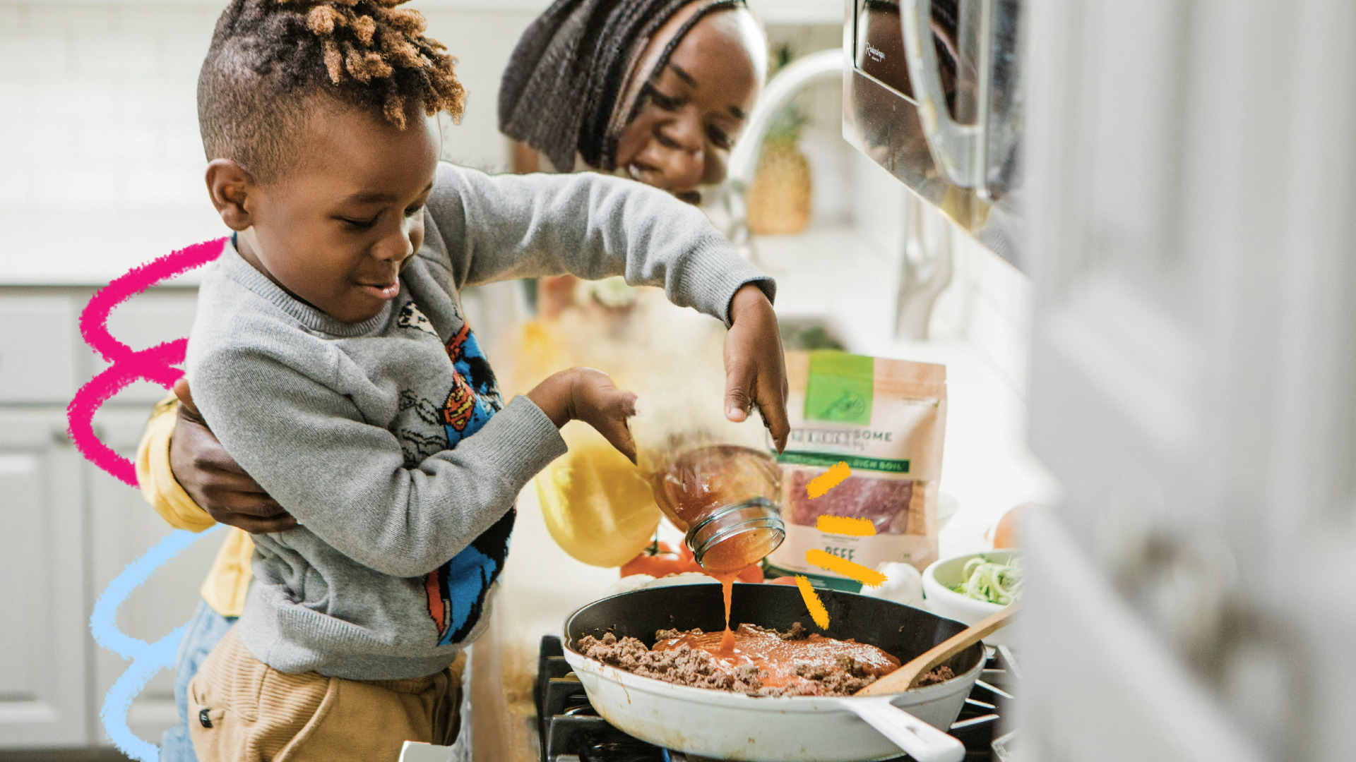Imagem mostra uma mãe e uma criança na cozinha. Um menino negro e uma mulher negra estão preparando uma comida com panelas e talheres.