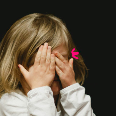 Imagem de capa de matéria sobre as diferenças enter bullying ou birra mostra uma menina branca de cabelos lisos com as mãos no rosto.