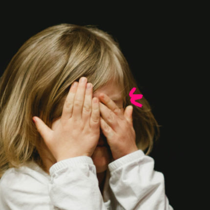 Imagem de capa de matéria sobre as diferenças enter bullying ou birra mostra uma menina branca de cabelos lisos com as mãos no rosto.