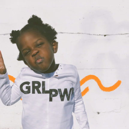 Meninas brincam menos: Imagem mostra uma menina negra, de cabelos crespos amarrados, vestido um moleton branco.