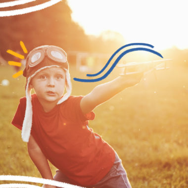 Imagem mostra criança brincando ao ar livre em um campo gramado. Ela usa um chapéu de aviador e segura um avião de brinquedo.