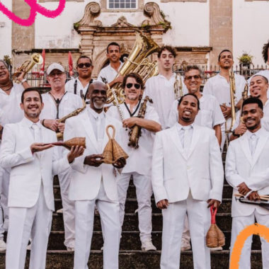 Imagem mostra 17 homens, todos vestidos de branco, e segurando um instrumento musical. Eles fazem parte da Orquestra Rumpilezz, de Salvador. Projeto da orquestra une educação, imaginação e música.