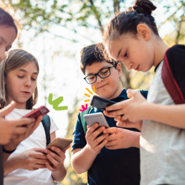 Imagem mostra quatro crianças lado a lado, ao ar livre. Cada uma está olhando para a tela de seu próprio celular. Todas carregam mochilas e parecem concentradas nos aparelhos, sem interagir entre si. A cena acontece em um ambiente com árvores ao fundo e luz do sol filtrada. Pequenos desenhos coloridos foram adicionados perto dos celulares.