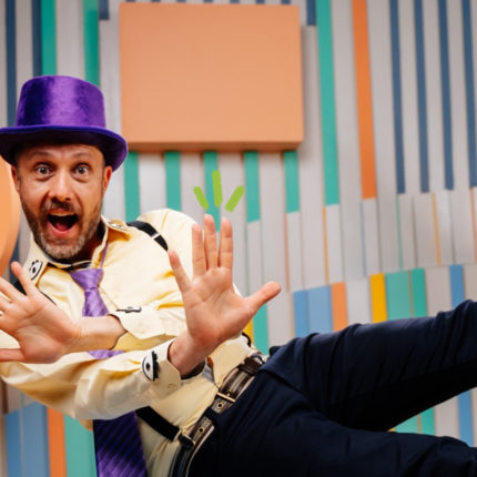 Imagem de capa de matéria sobre tédio nas férias mostra Nélio Sprea, um homem branco, com chapéu roxo e roupa amarela pulando.