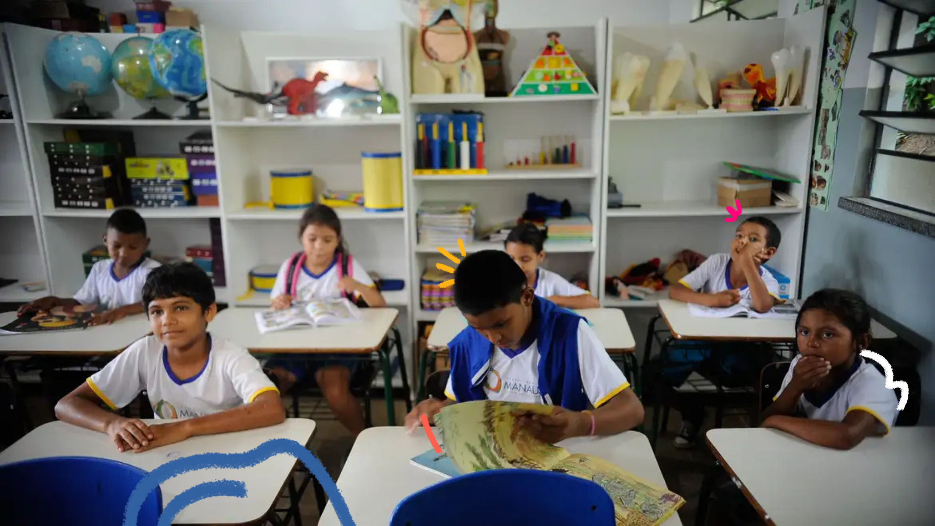 Crianças em sala de aula, sentadas em carteiras, com livros abertos e materiais escolares ao fundo.