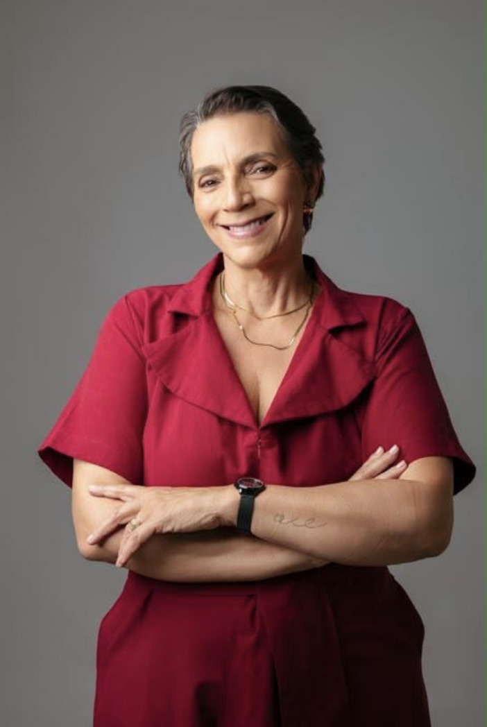 Monalisa Barros, psicóloga, posa sorrindo, com os braços cruzados, usando uma roupa vermelha diante de um fundo cinza.
