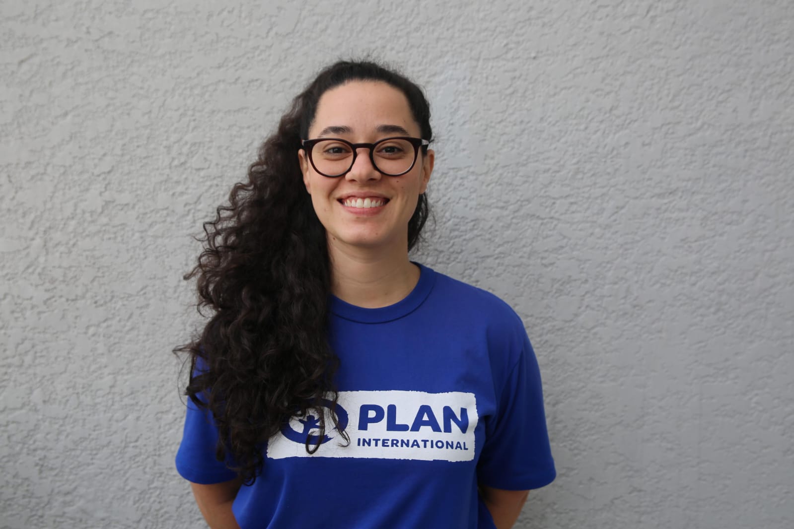 Paula Alegria, coordenadora de advocacy e direitos reprodutivos da Plan International, posa diante de uma parede cinza.