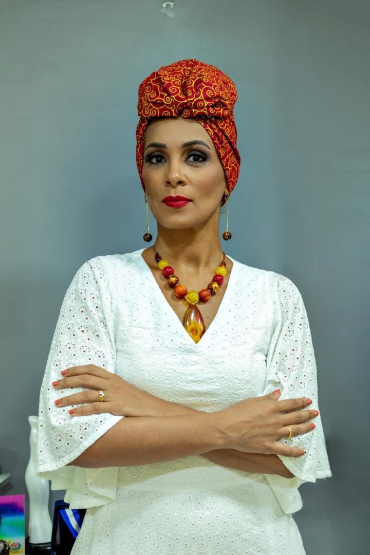 Lívia Sant’Anna Vaz posa para a foto com turbante vermelho estampado, vestido branco e colares coloridos.