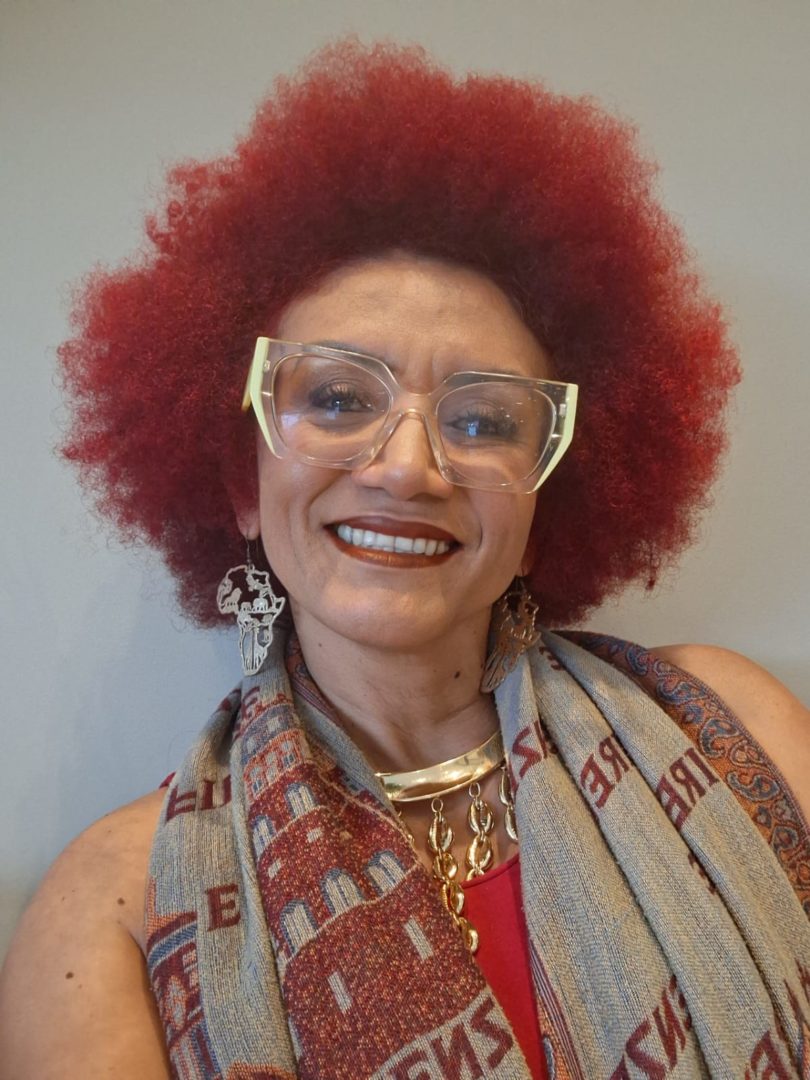 Retrato de Odailta Alves, com cabelo afro vermelho, óculos e lenço estampado.